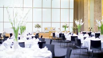 A banquet hall with round tables set for dining, a stage with a sofa, and floral centerpieces.