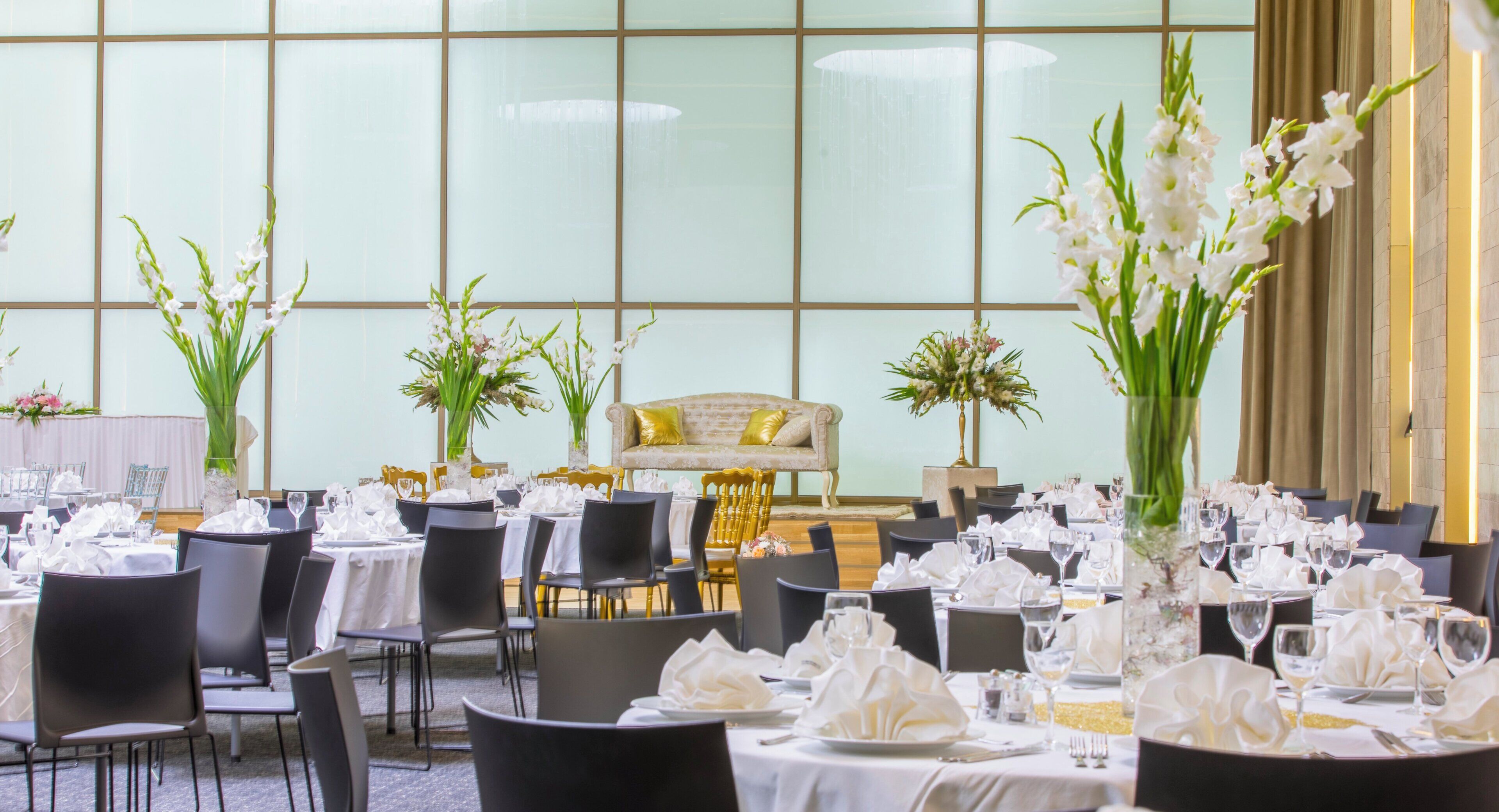 Un salón de banquetes con mesas redondas dispuestas para comer, sillas y centros de mesa florales.
