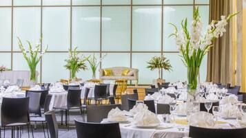 Un salón de banquetes con mesas redondas dispuestas para comer, sillas y centros de mesa florales.