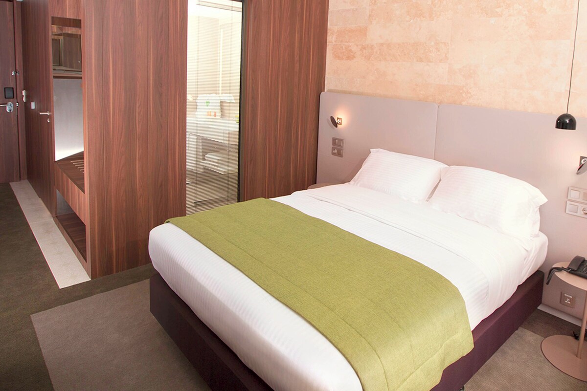 A hotel room with a bed, bedside table, and a red chair.