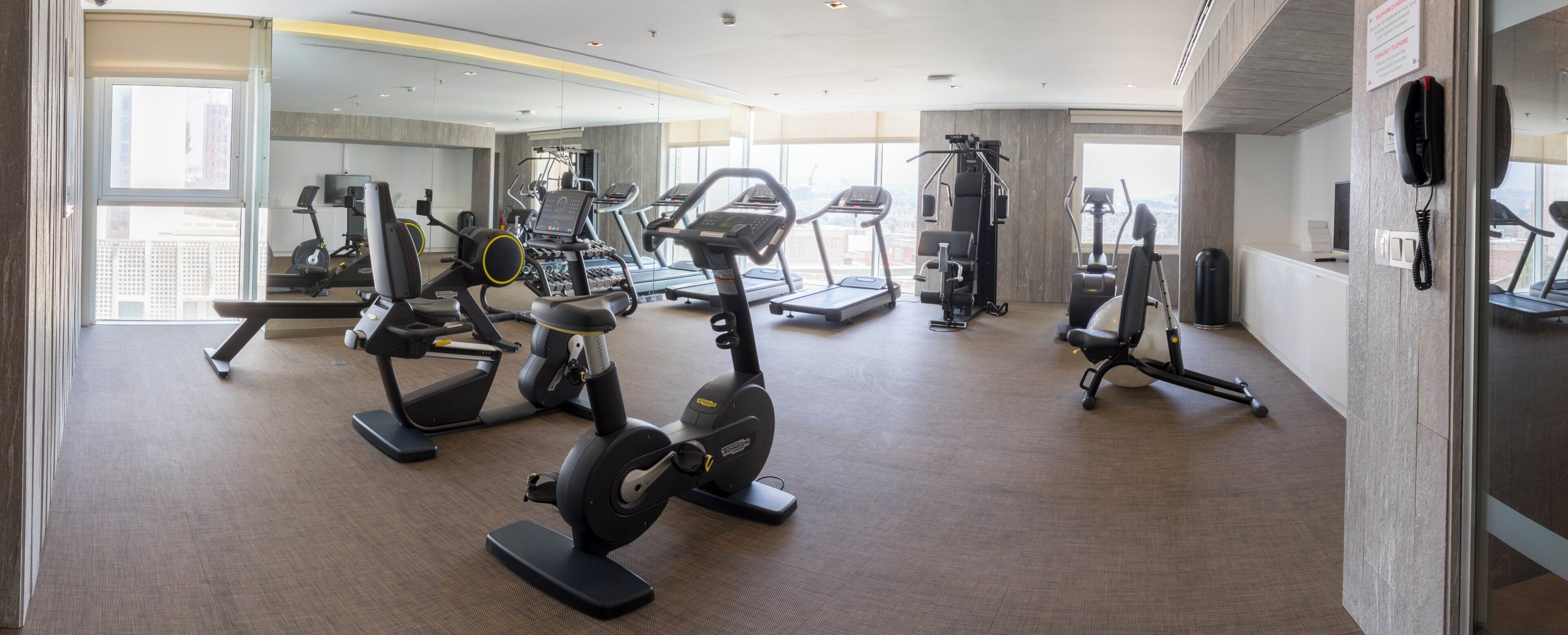 Un gimnasio con diversos equipos de ejercicio, amplias ventanas y un diseño interior moderno.