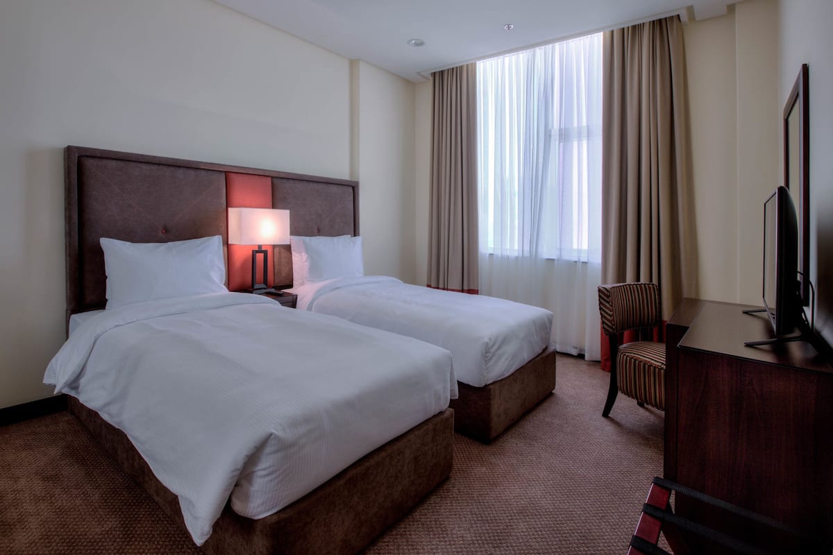 Une chambre d’hôtel avec deux lits, un bureau, une chaise et un téléviseur.
