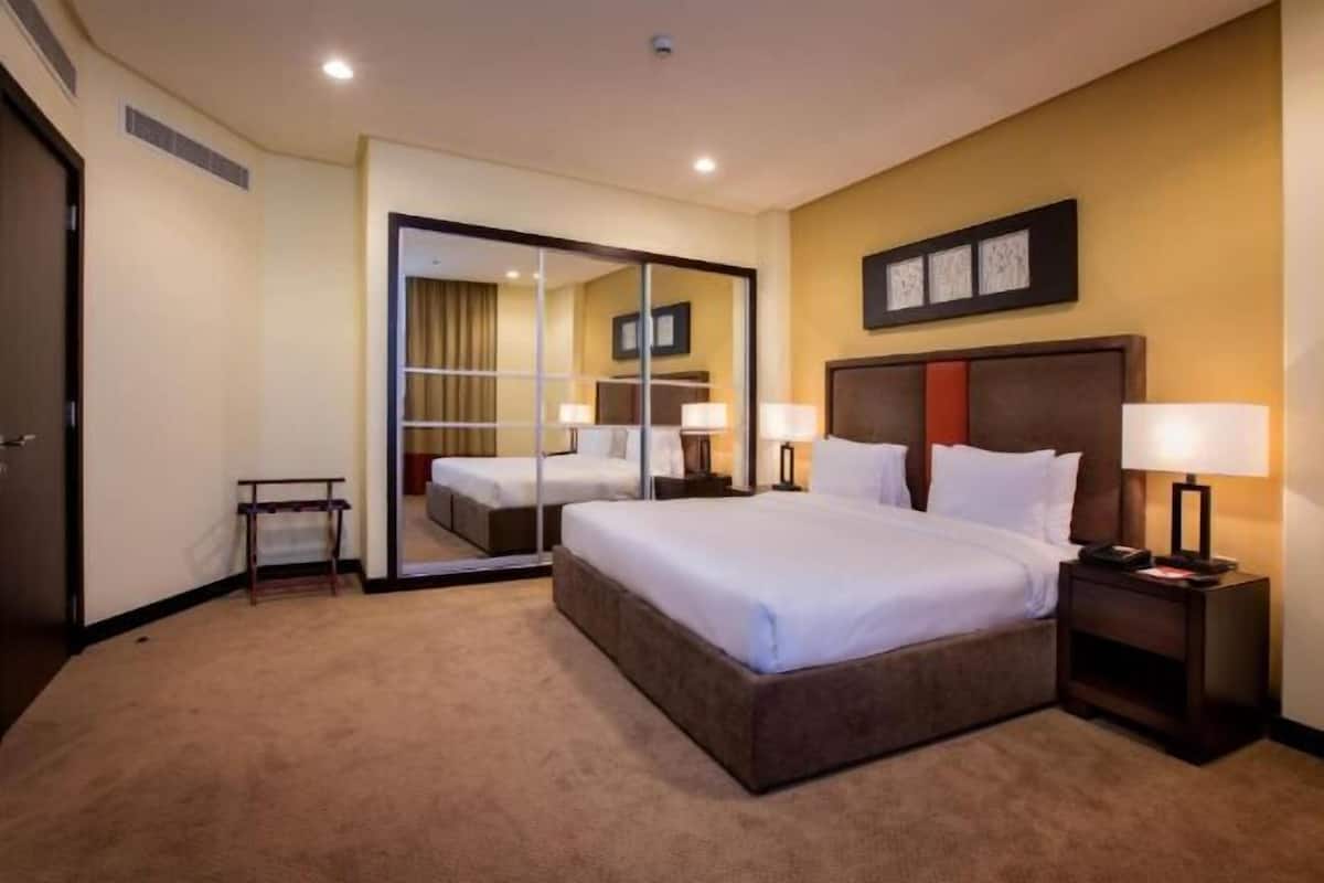 Une chambre d’hôtel avec un grand lit, des tables de chevet, un miroir et un tableau encadré au mur.