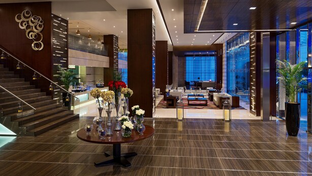 A modern hotel lobby with a grand staircase, a reception desk, and a seating area. - Rosh Olaya Hotel (Riyadh)