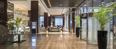 A modern lobby with a reception desk, seating area, and large potted plants.