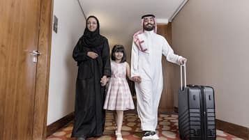A hotel hallway with wooden doors, a patterned carpet, and a black suitcase.