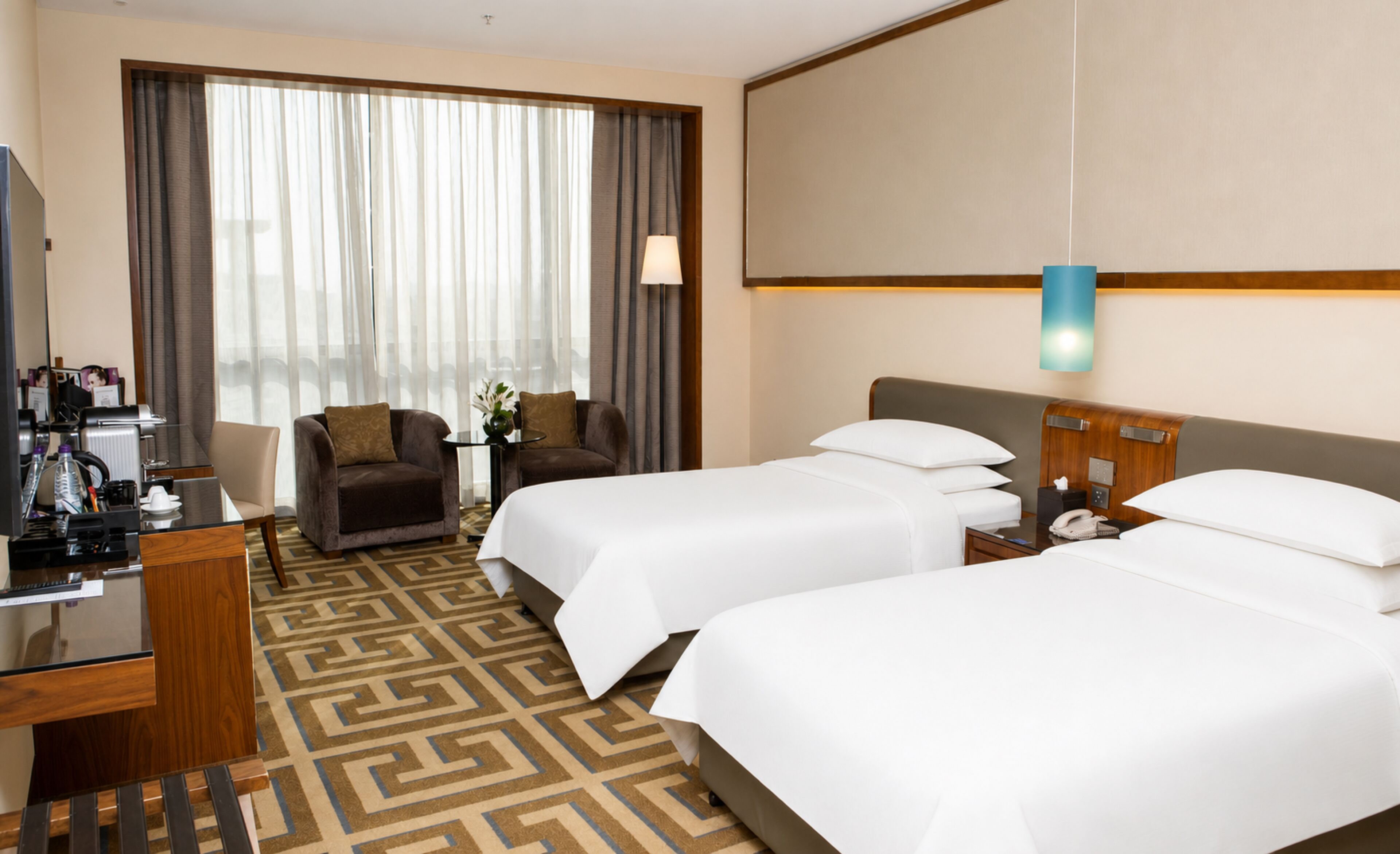 A hotel room with two beds, a desk with a telephone, a chair, and a coffee machine.