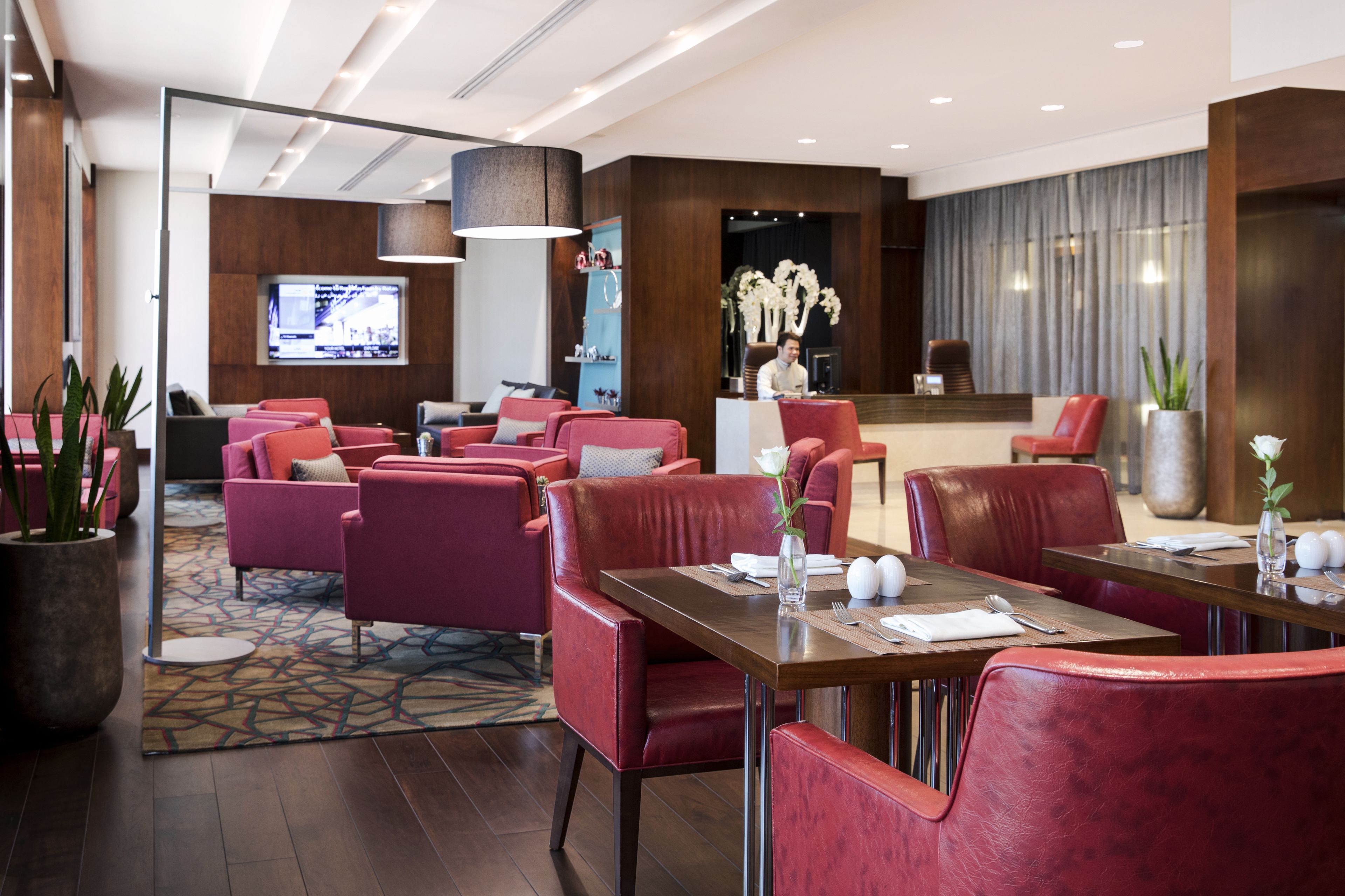 A hotel lobby with red seating, a reception desk, and a TV screen.