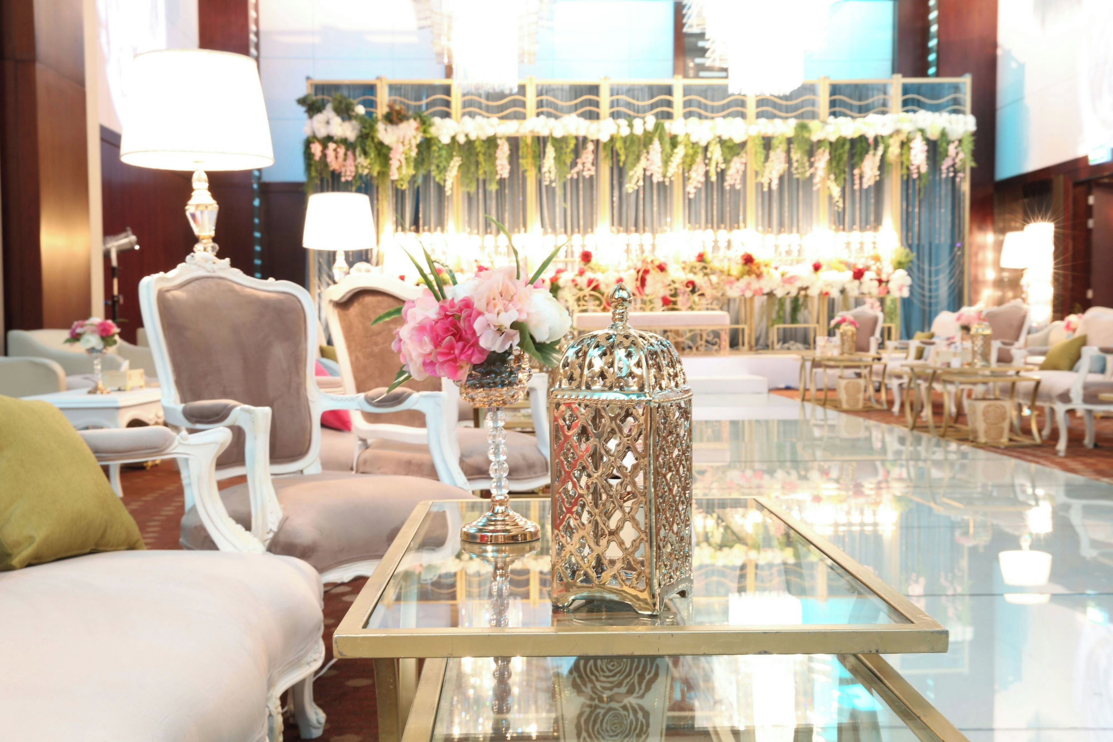 Un salón luminoso y elegantemente amoblado con asientos cómodos, una mesa de vidrio y arreglos florales decorativos.