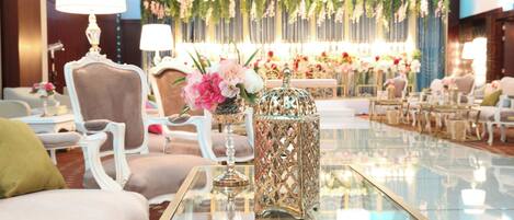 Un salón luminoso y elegantemente amoblado con asientos cómodos, una mesa de vidrio y arreglos florales decorativos.