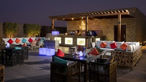 An outdoor bar area with wicker furniture and a stone wall backdrop. - Rosh Olaya Hotel (Riyadh)
