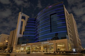 A modern hotel with a curved glass facade and a prominent entrance. - Rosh Olaya Hotel (Riyadh)