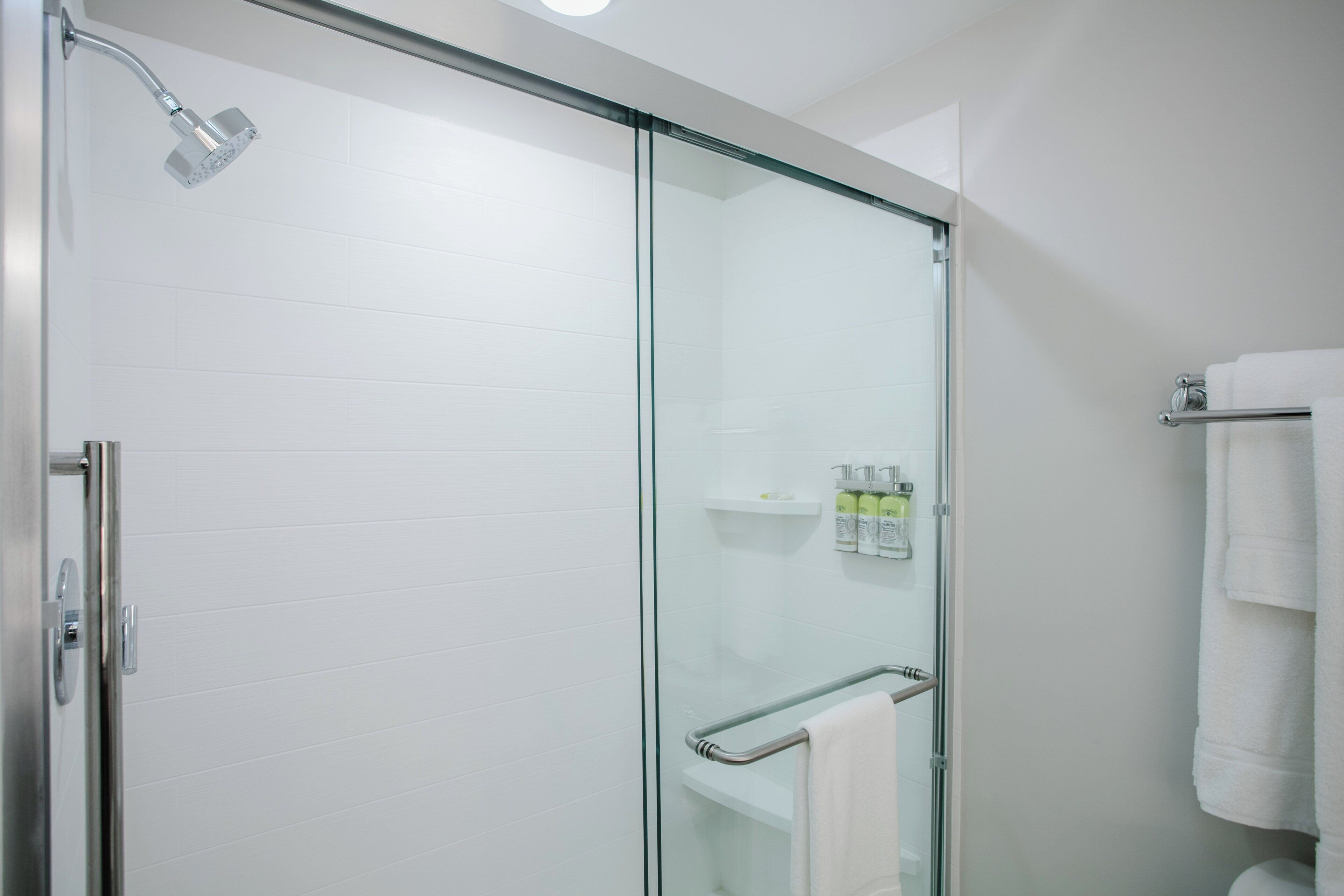 A modern bathroom with a glass-enclosed shower, a glass door, a towel rack, and a shelf with toiletries.