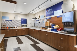 A modern kitchen area with a breakfast bar, labeled sections for bakery, cereal, and fruit, and a beverage dispenser. - Holiday Inn Express & Suites Oakhurst - Yosemite Park Area by IHG (Oakhurst)