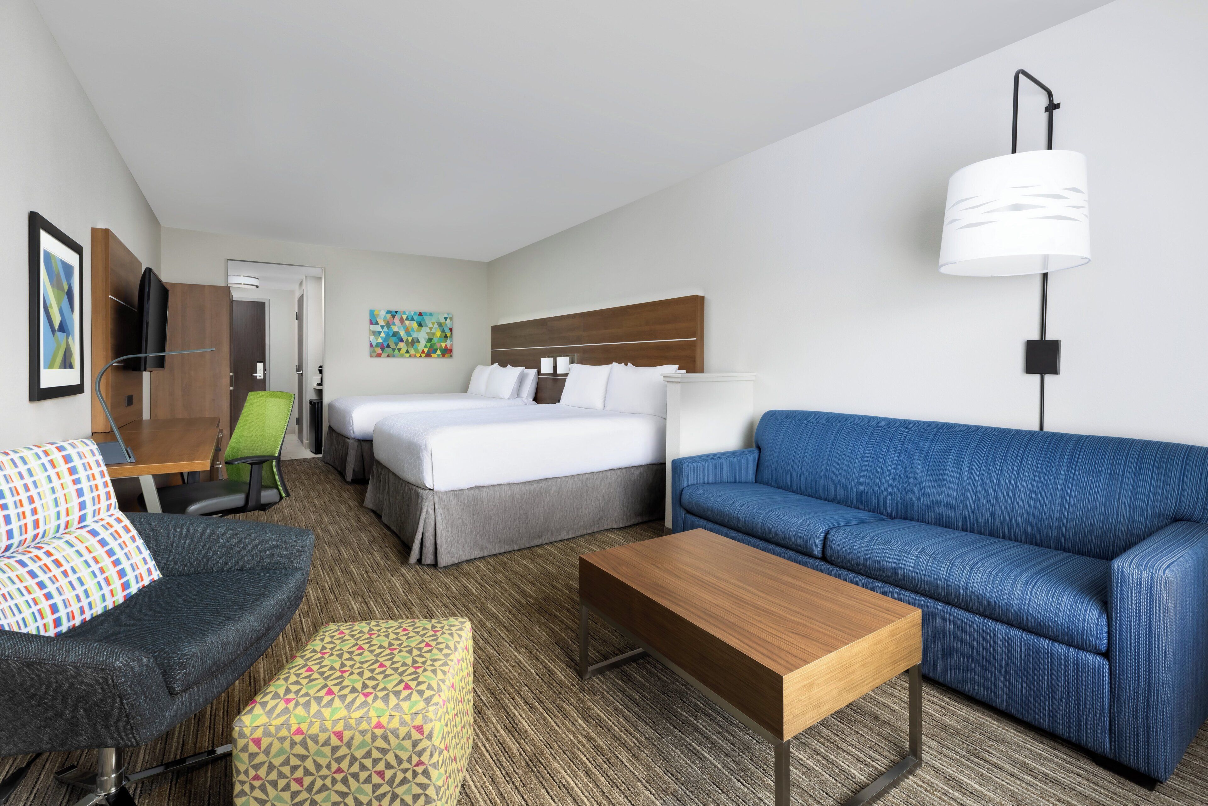 A hotel room with a bed, a sofa, a desk, a chair, and a TV.