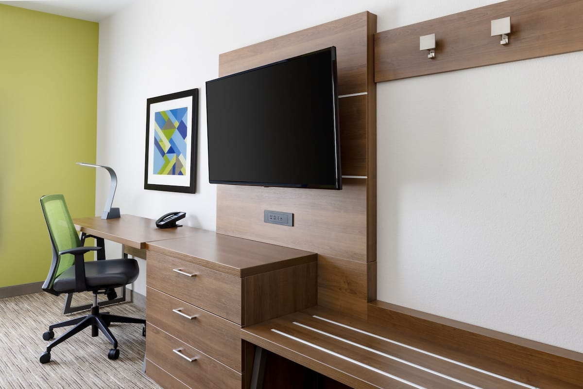 A modern office desk with a flat-screen TV, a green chair, and a framed artwork on the wall.