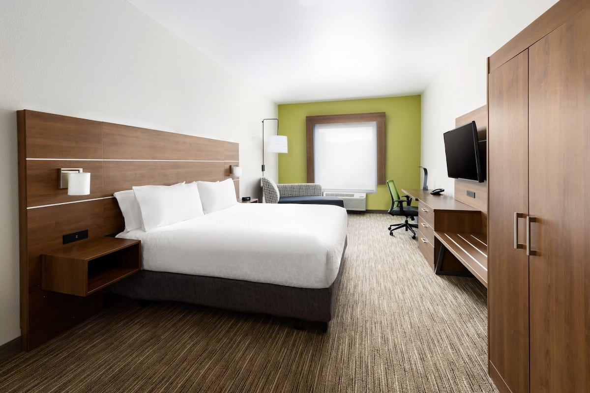A hotel room with a large bed, a desk, a chair, a television, and a wardrobe.