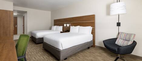 A hotel room with a large bed, two bedside tables, a desk with a chair, a lamp, and a chair with a patterned cushion.