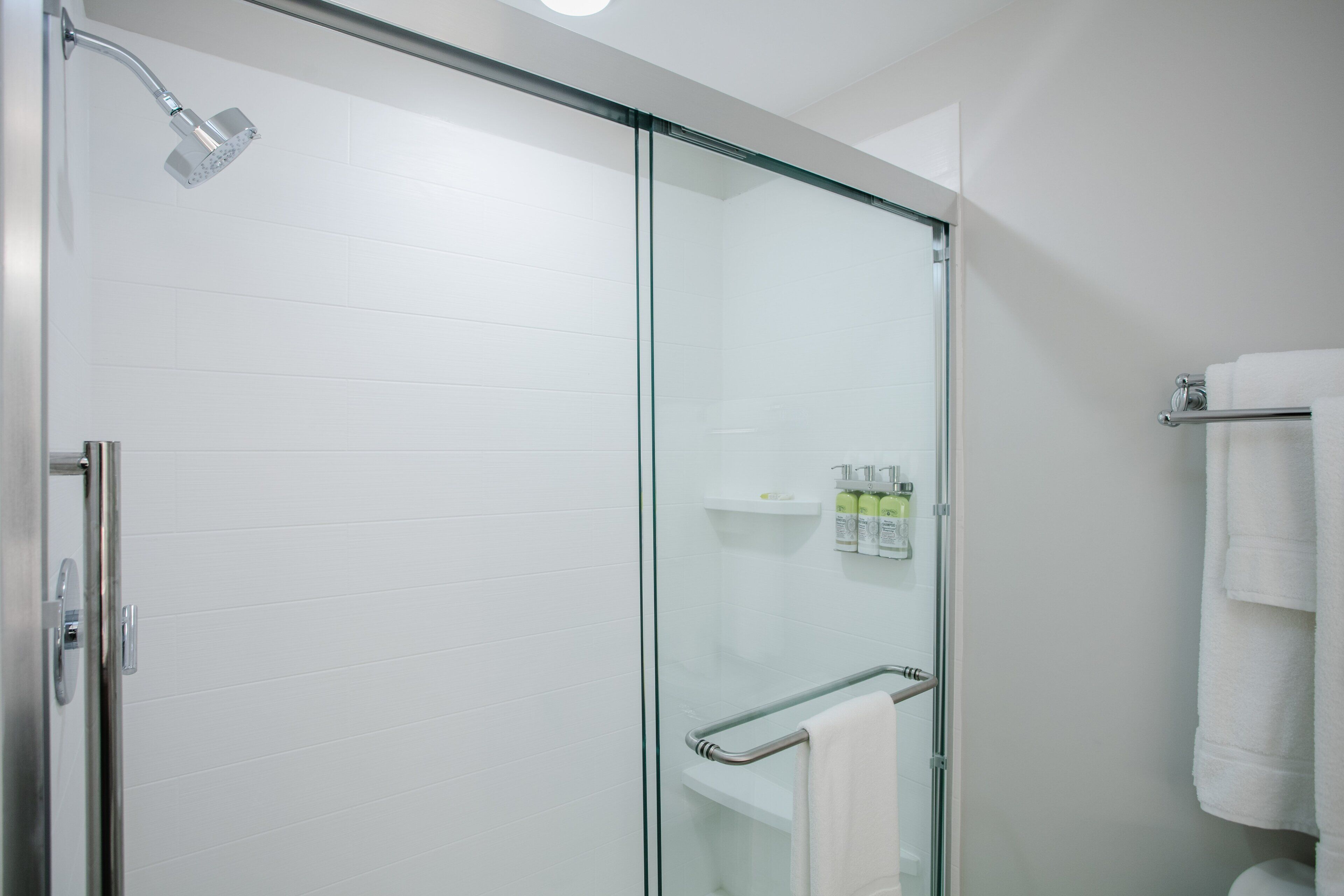 A modern bathroom with a glass shower enclosure, a glass door, a glass partition, and a towel rack with towels.