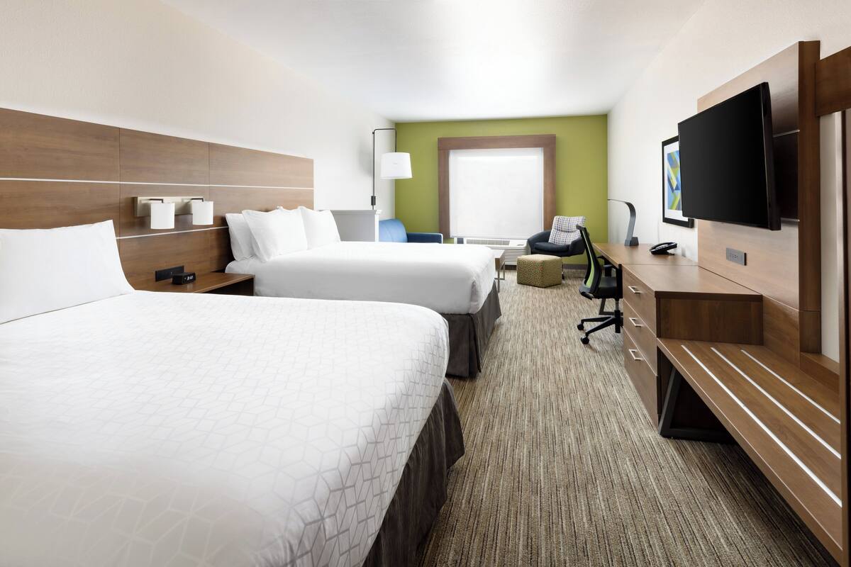 A hotel room with two beds, a desk, a chair, a TV, and a window.