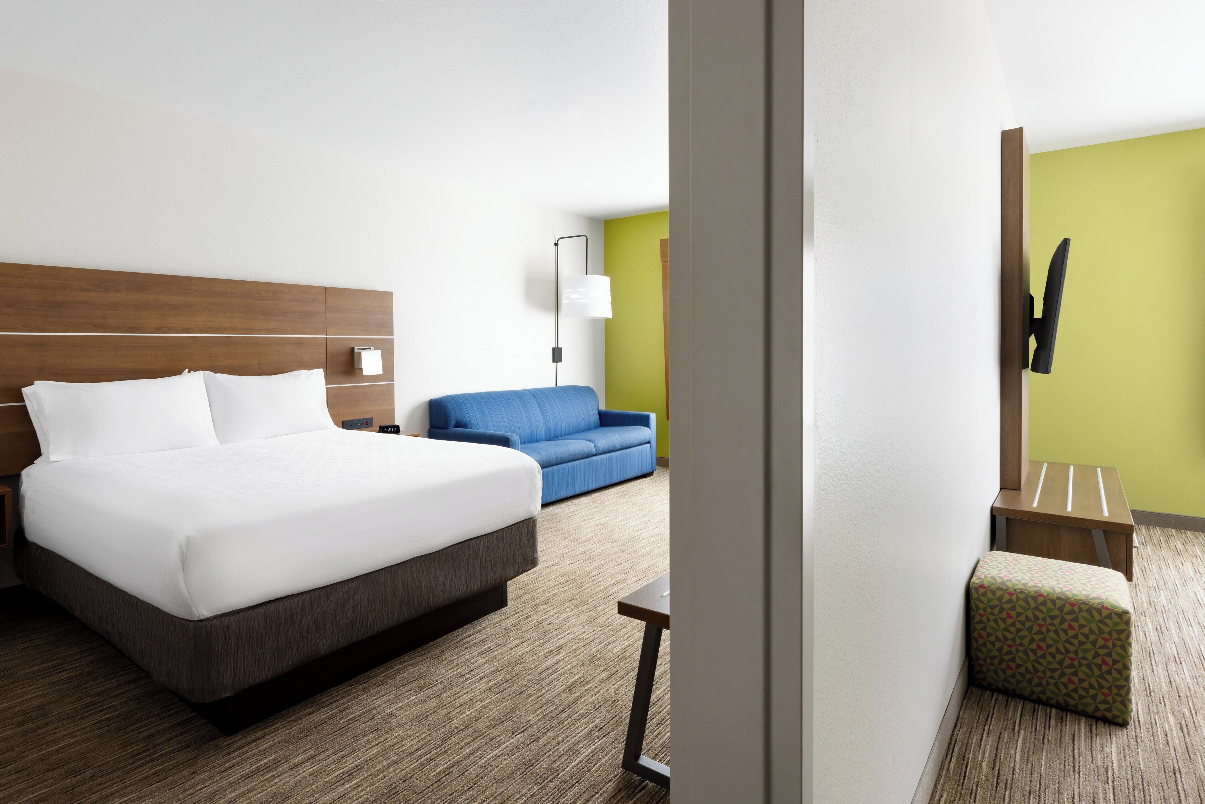 A hotel room with a large bed, a blue sofa, a small table, and a TV mounted on the wall.