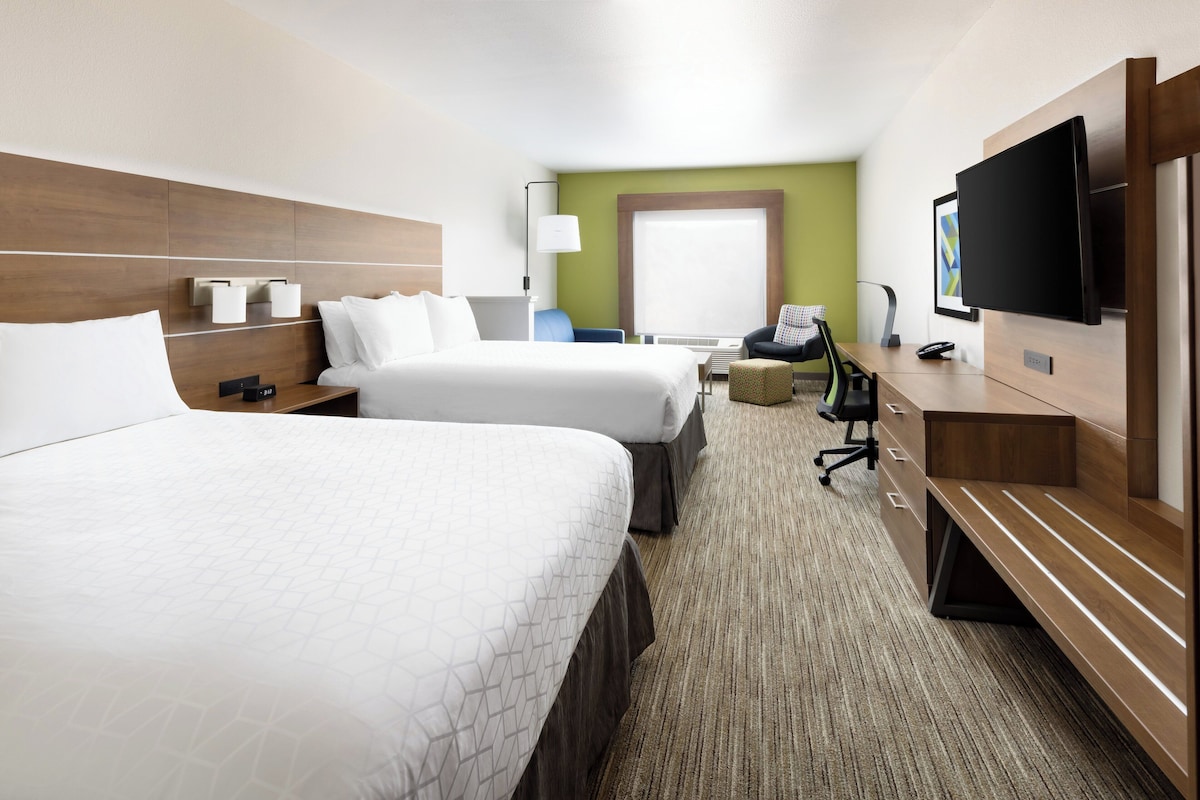 Une chambre d’hôtel avec deux lits, un bureau, une chaise, une télévision et une fenêtre.