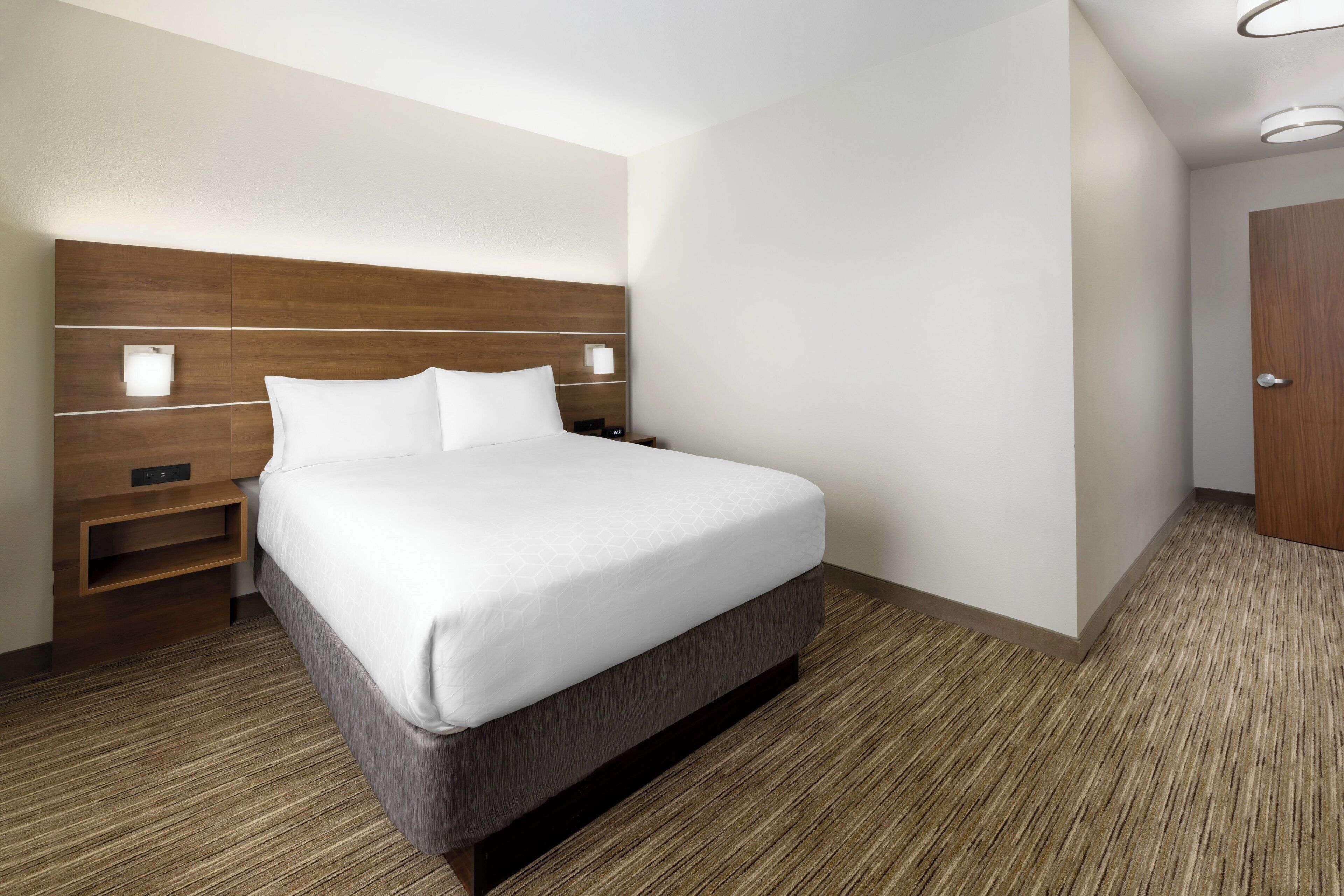 A hotel room with a large bed, bedside tables, a wooden headboard, and a door.