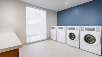 A laundry room with four front-loading washing machines, a large window, and a white countertop.