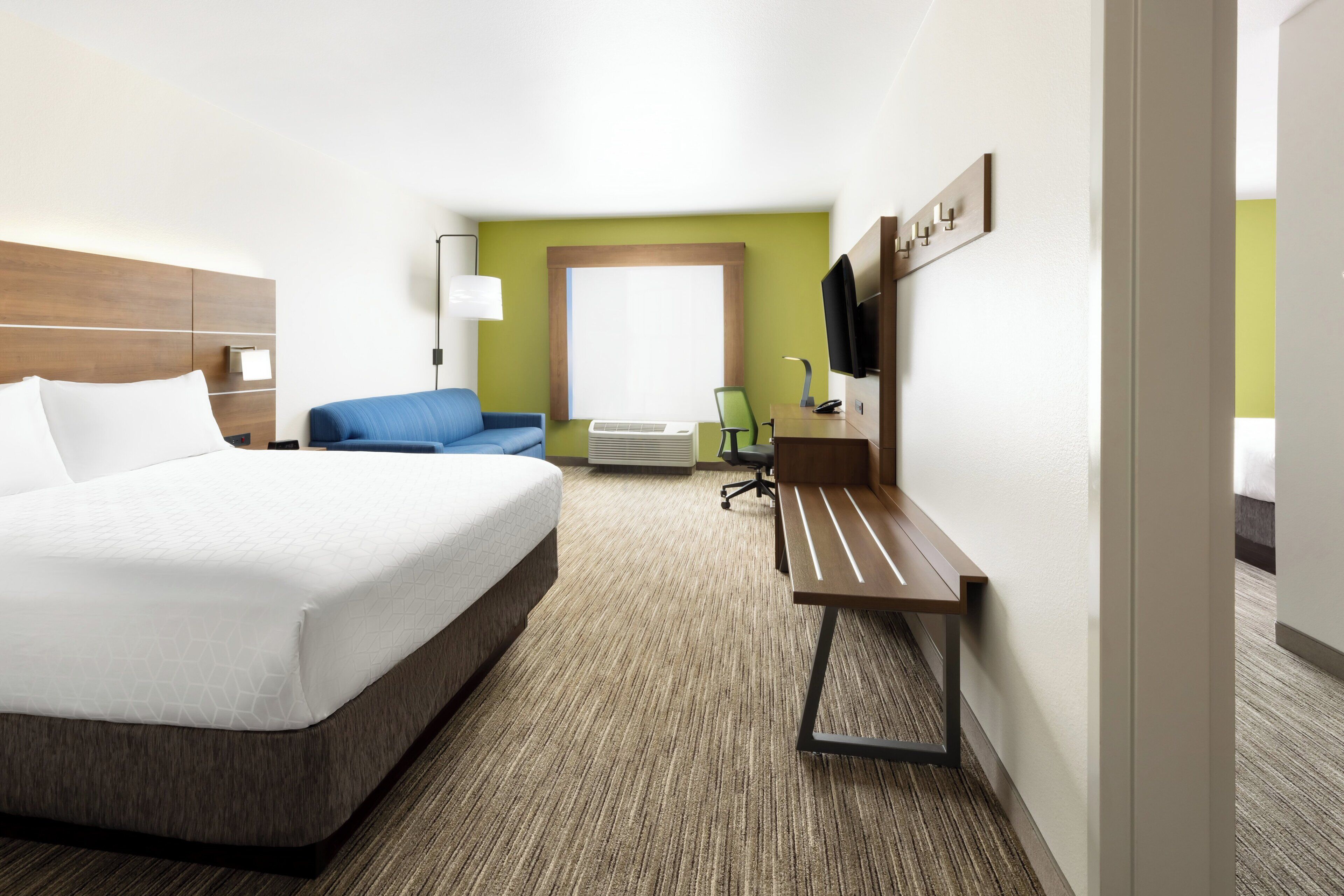A hotel room with a bed, a desk, a chair, a TV, and a window.