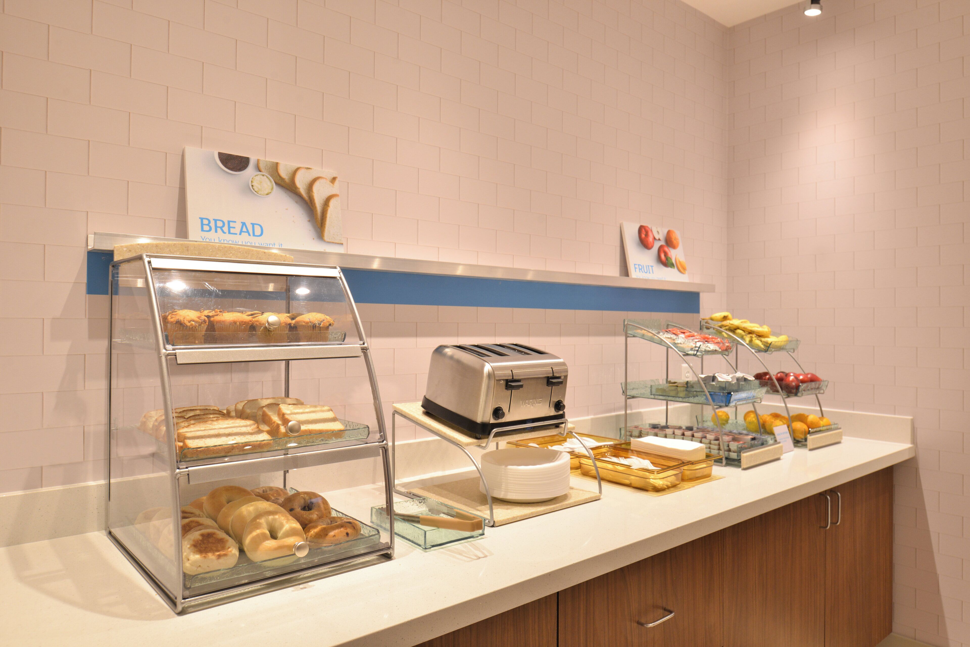 A breakfast buffet with bread, pastries, fruits, and a toaster.