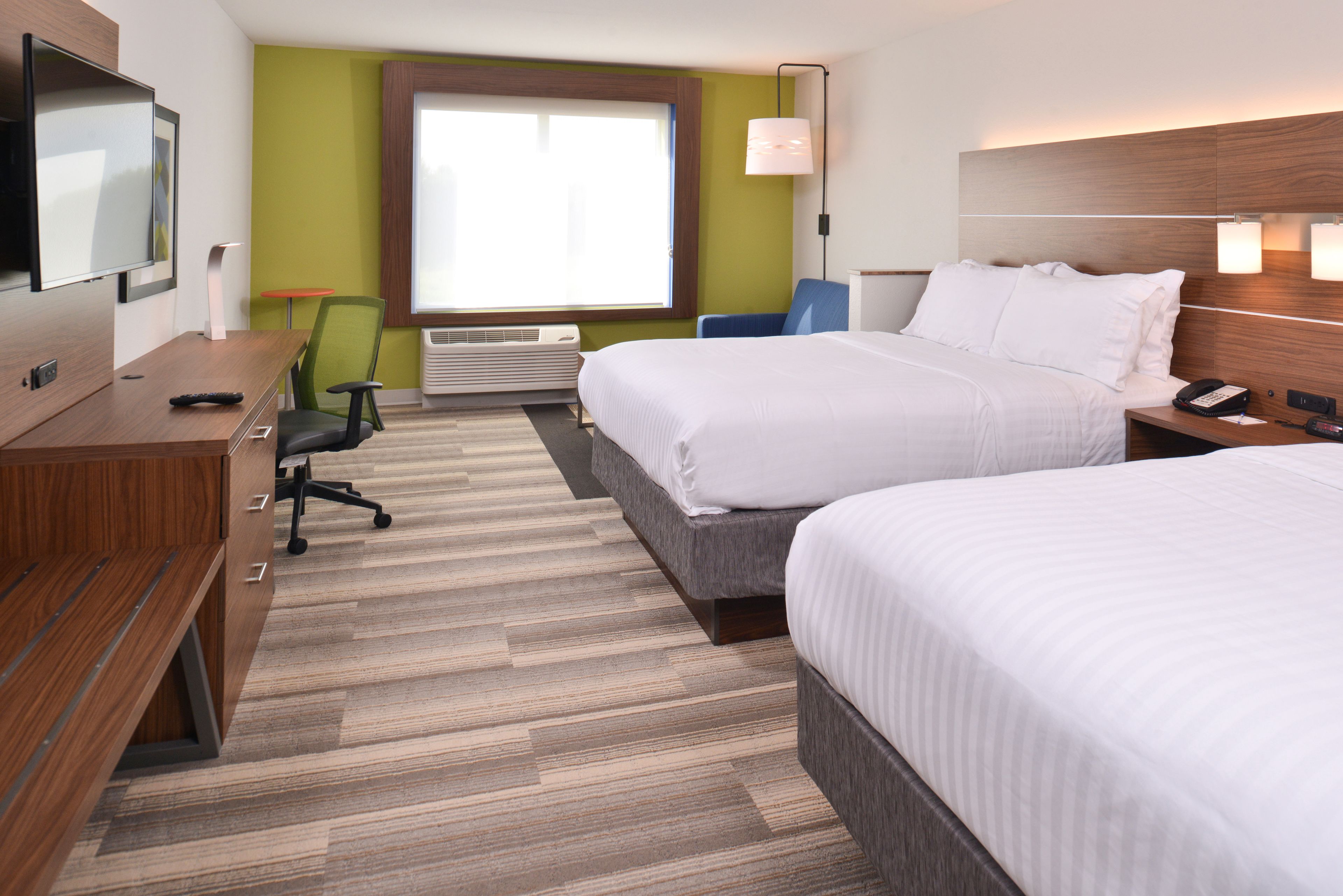 A hotel room with two beds, a desk, a chair, a TV, and a window with a view.
