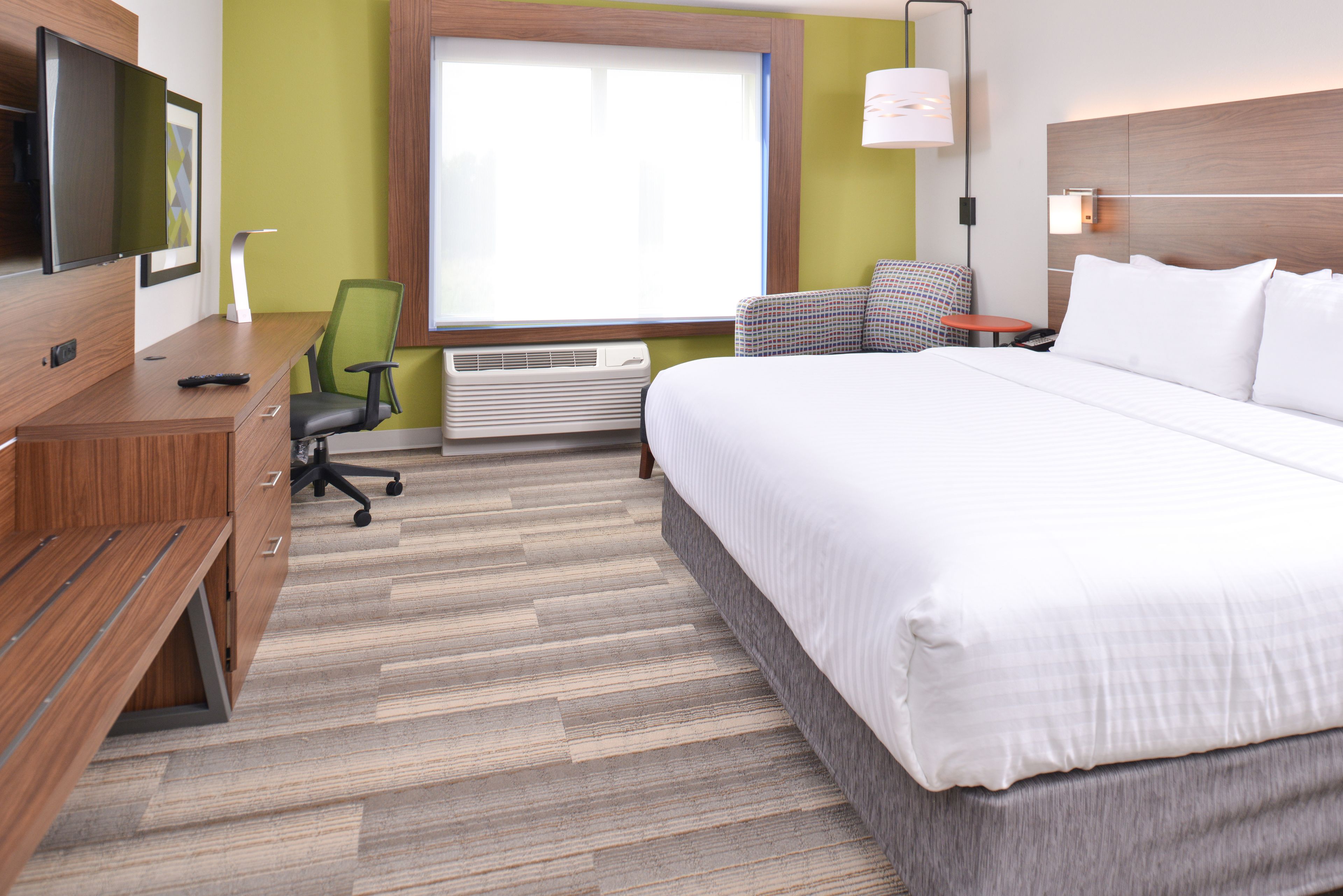 A hotel room with a bed, desk, chair, TV, and window.