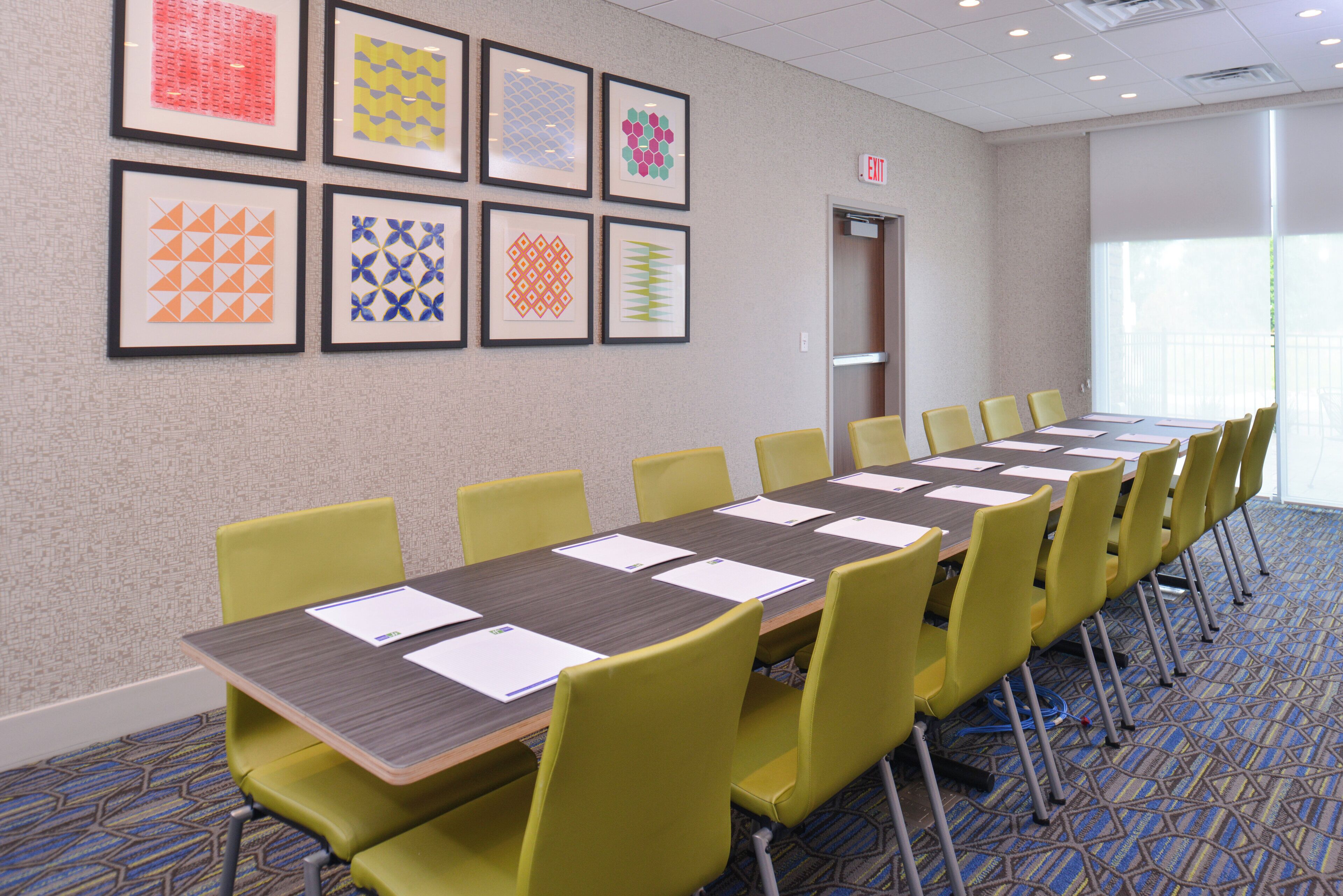 A conference room with a long table, yellow chairs, and framed artwork on the wall.