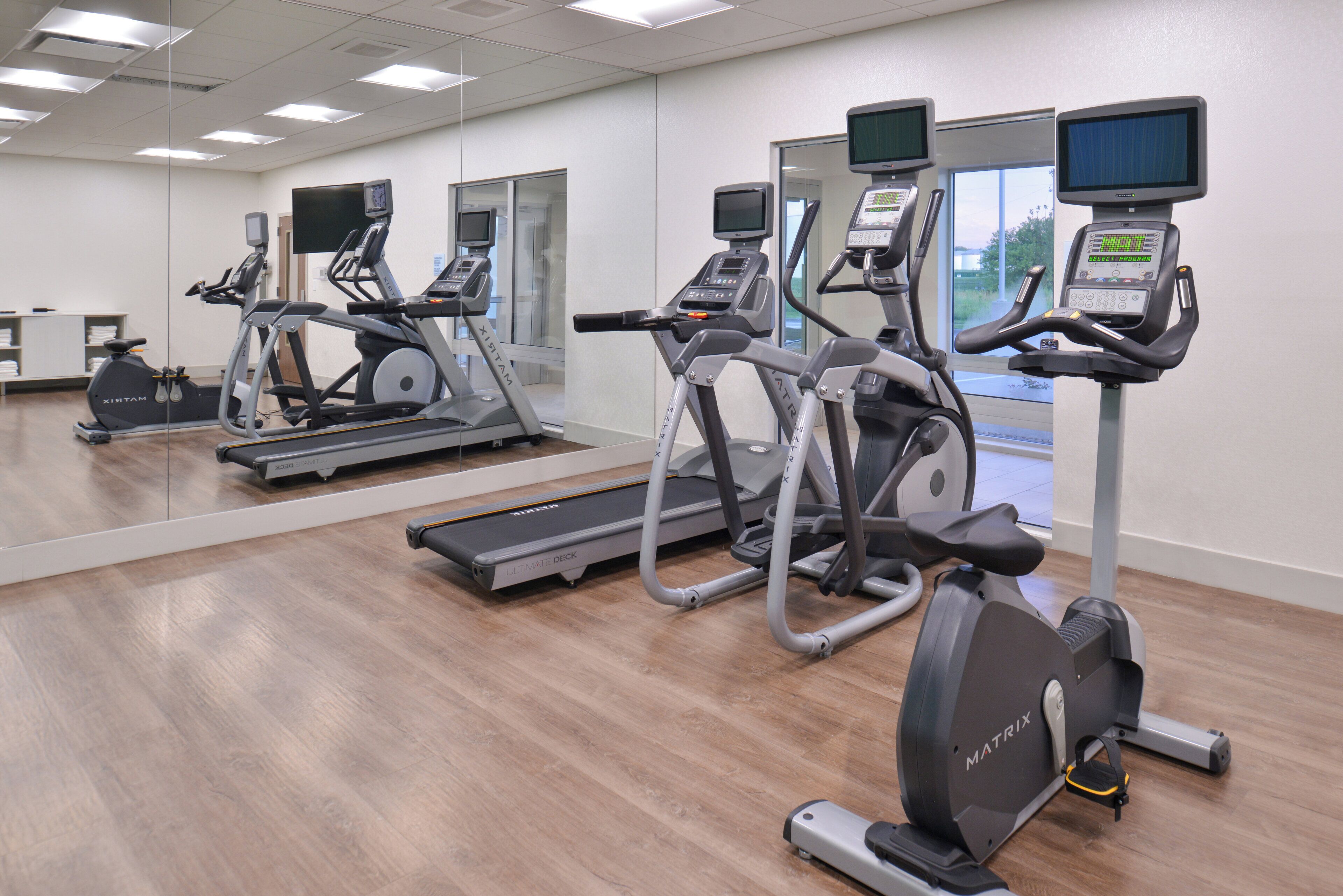 A gym with multiple exercise machines, including treadmills and stationary bikes, and a mirrored wall.