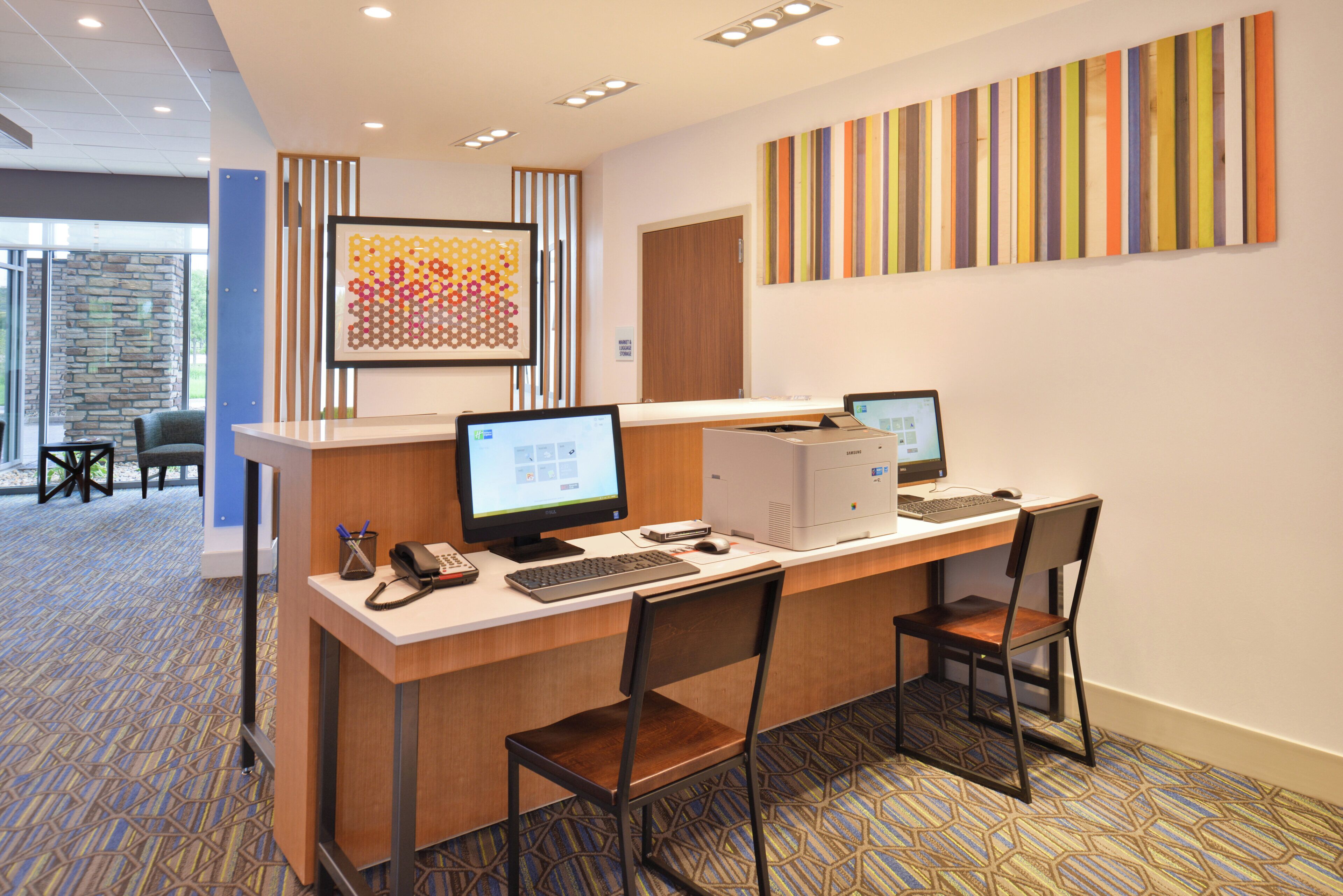 A reception desk with two computer monitors, a phone, and a keyboard. There are two chairs in front of the desk.