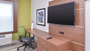Ein moderner Arbeitsraum mit einem Holztisch, einem grünen Bürostuhl, einem Wand-Fernseher und einem gerahmten abstrakten Kunstwerk an der Wand.