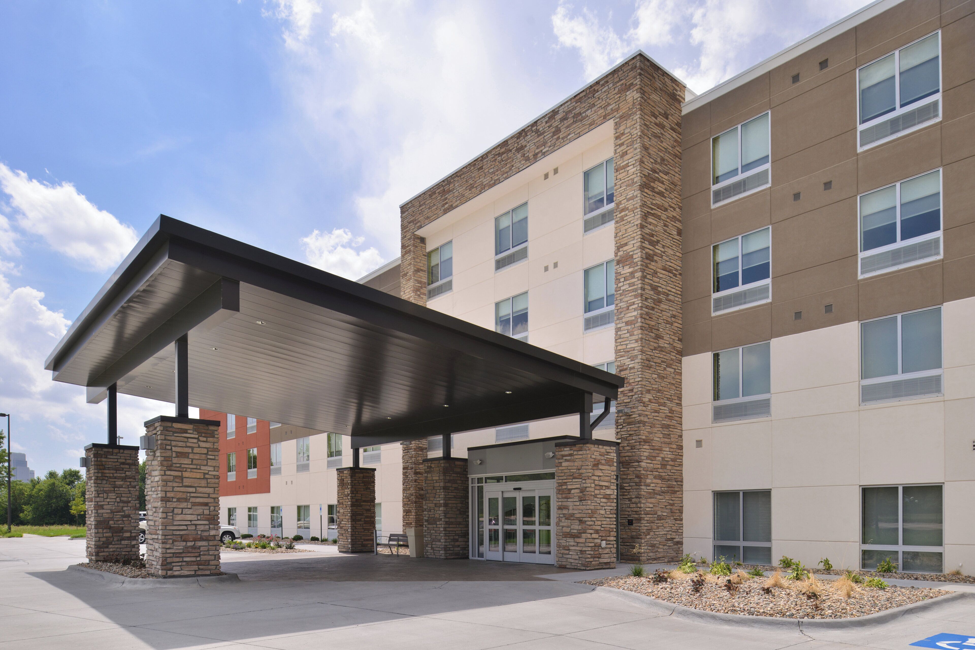 A modern building with a covered entrance, stone pillars, and a parking lot.
