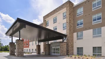 A modern building with a covered entrance, stone pillars, and a parking lot.