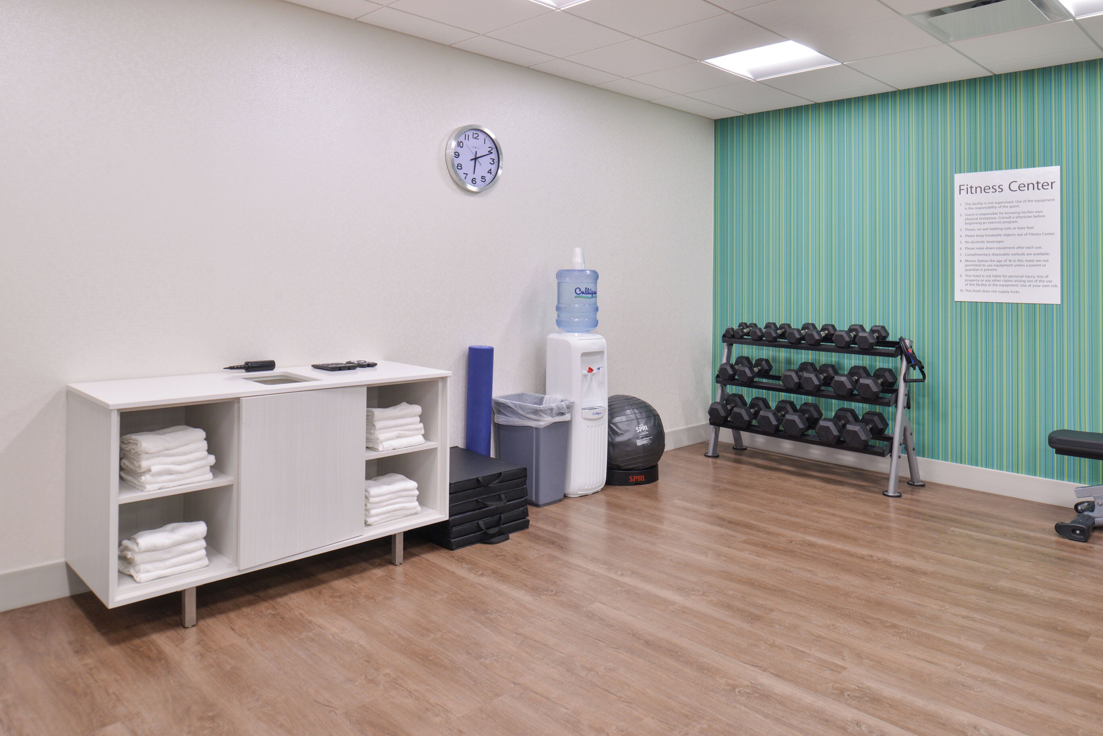 A fitness center with a water dispenser, dumbbells, and a sign listing rules.