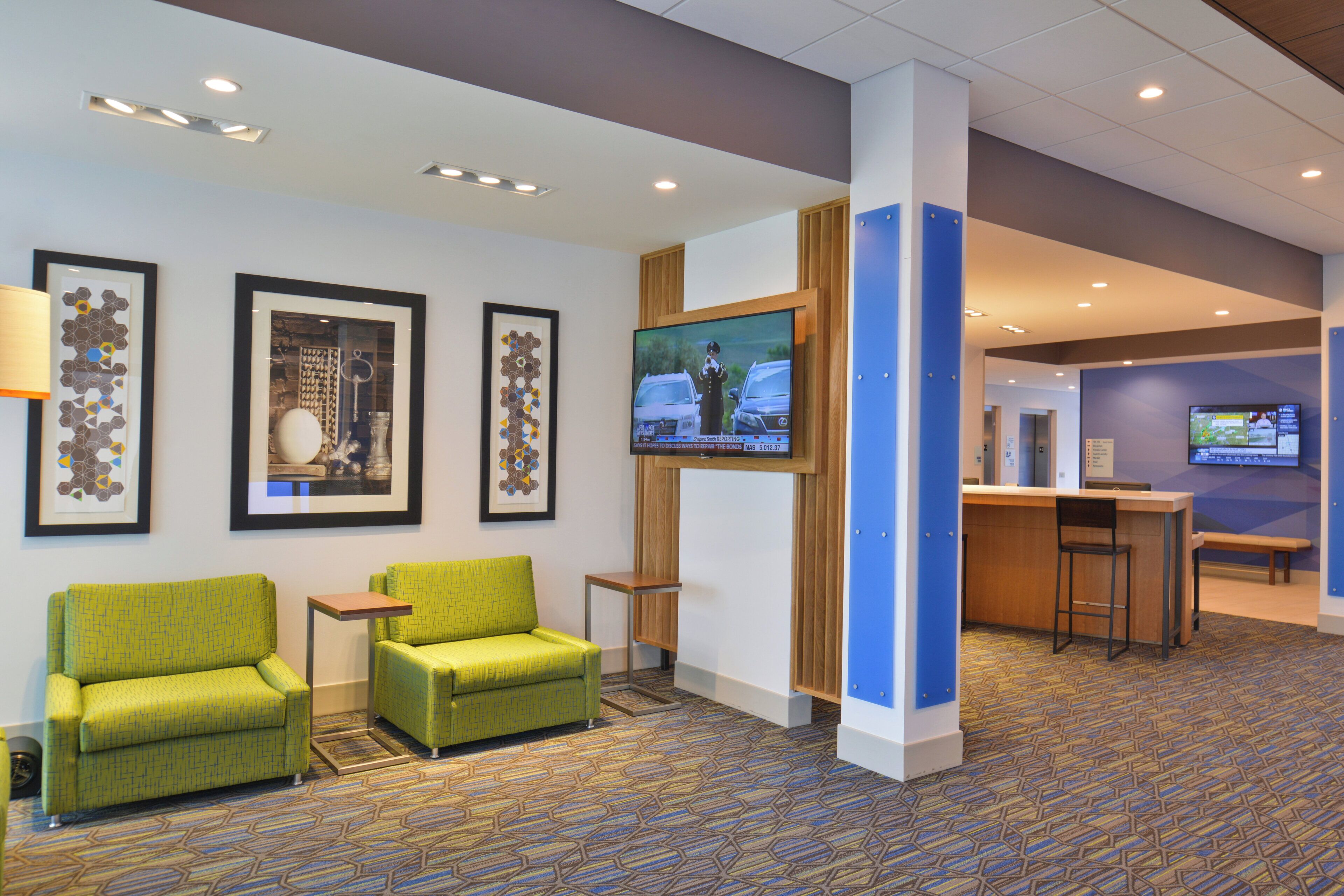 A lobby with green chairs, a TV screen, framed artwork, and a reception desk.