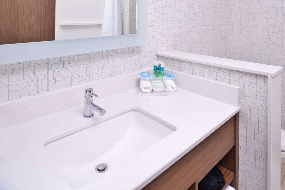 A bathroom with a white sink, a mirror, and a shelf with toiletries.