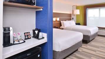 A hotel room with a kitchenette, two beds, a large window, and a view of the city skyline.