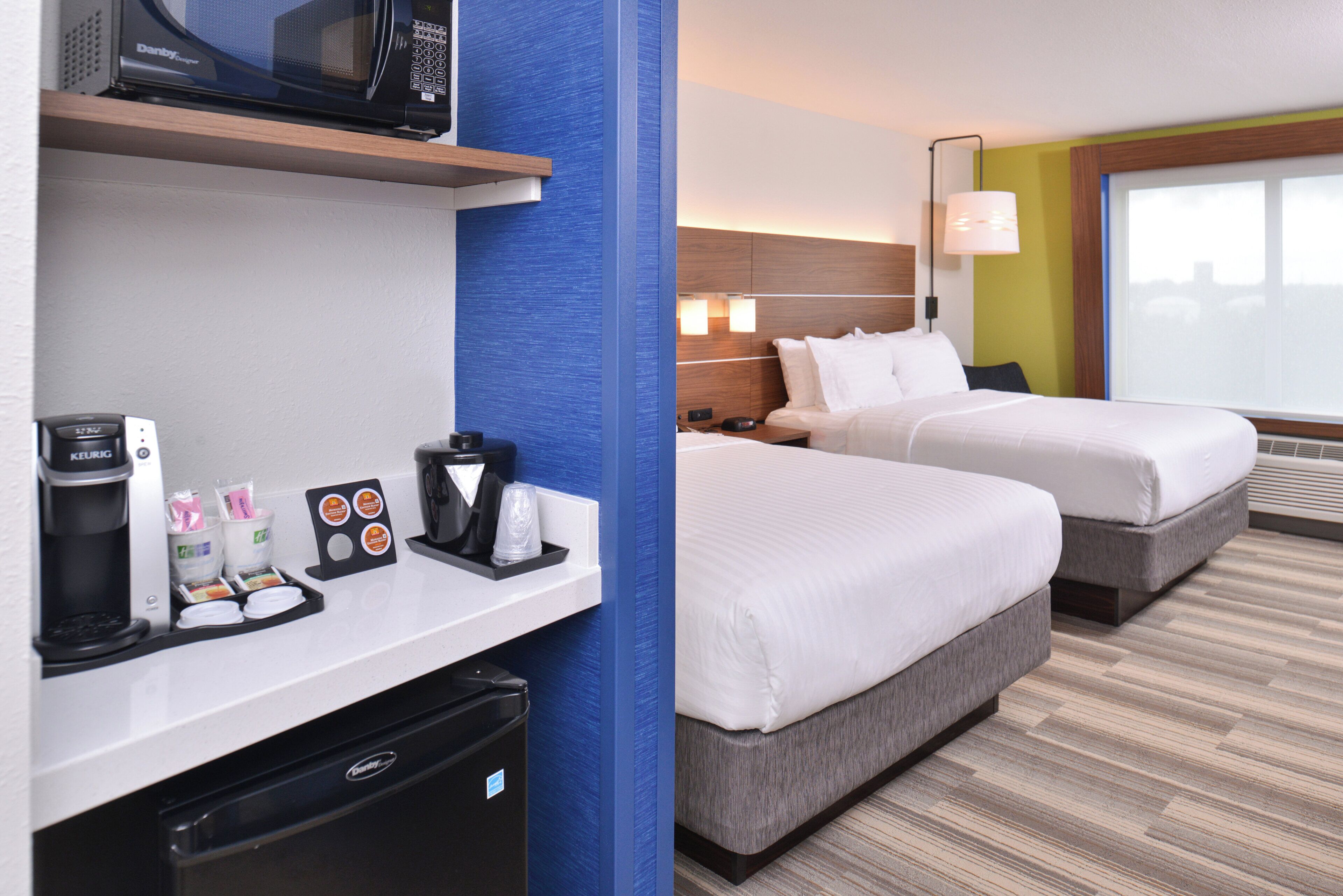 A hotel room with a minibar, a bed, a desk, and a window.