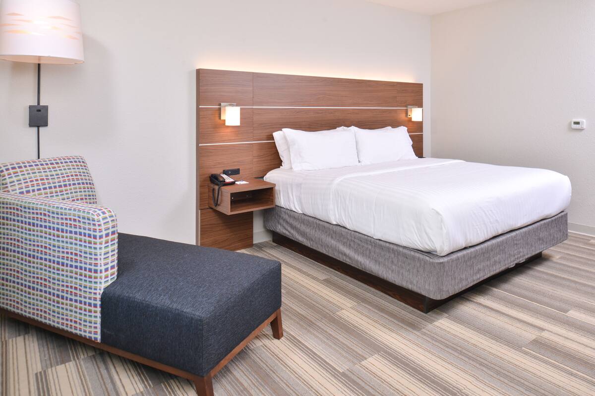 A hotel room with a bed, a chair, a nightstand, and a lamp.