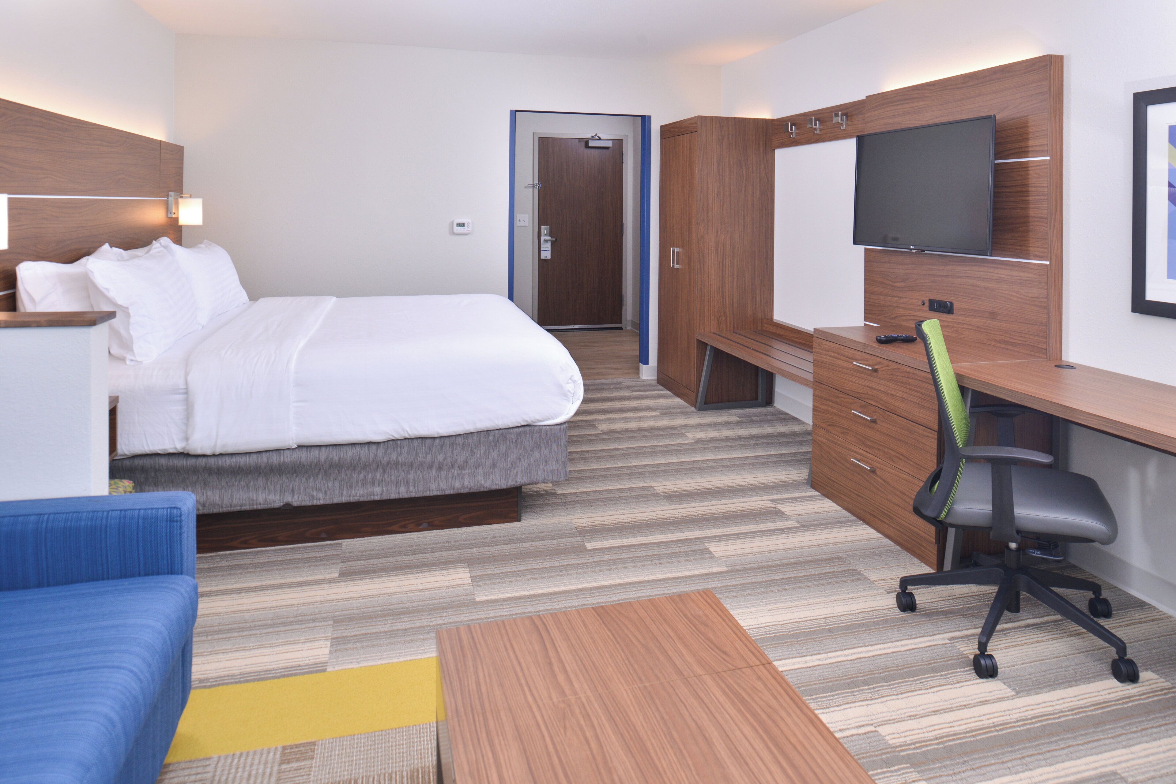 A hotel room with a bed, a desk, a chair, a television, and a blue sofa.