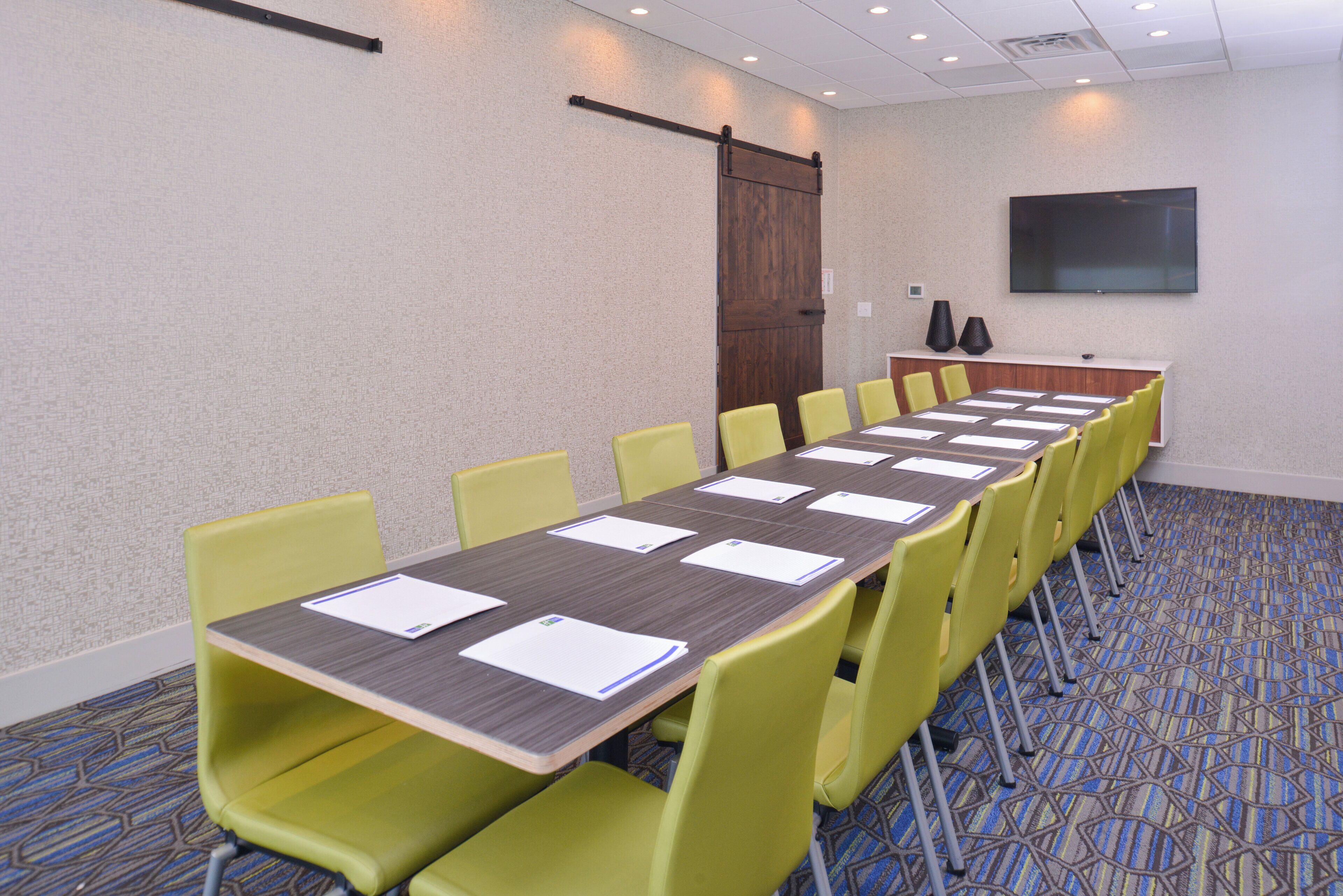 A conference room with a long table, yellow chairs, and a large screen on the wall.