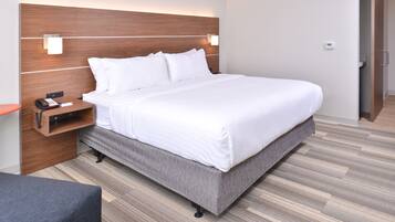Une chambre d’hôtel moderne avec un grand lit, une tête de lit en bois, des lampes de chevet, une table de chevet et un banc recouvert d’un tissu gris.