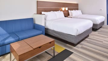 A hotel room with a blue sofa, two single beds, a wooden nightstand, and a small table.