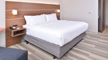 Quarto de hotel moderno com uma cama grande, uma mesinha de cabeceira com telefone e papéis, um criado-mudo e um guarda-roupa.