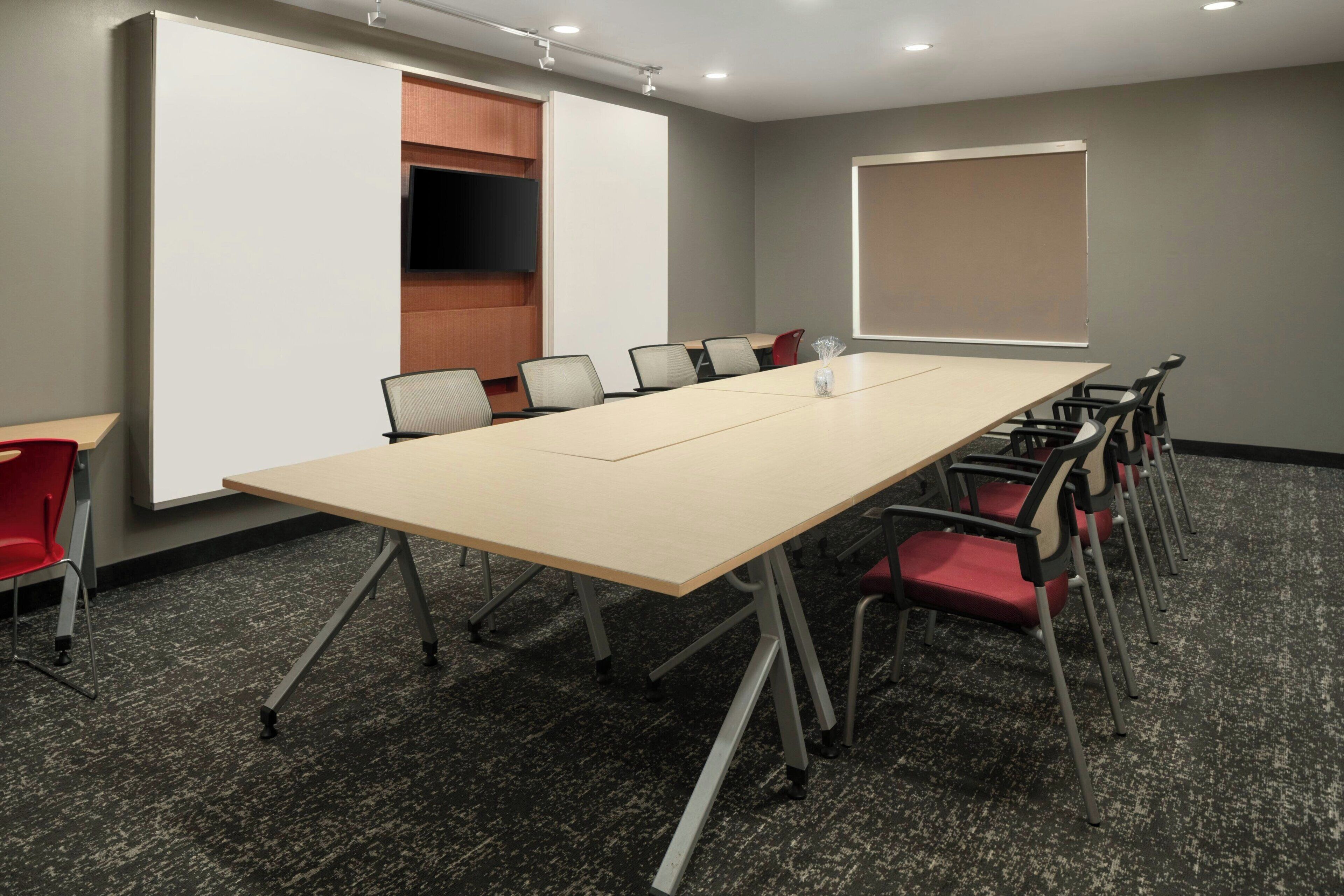 Un salón de conferencias con una larga mesa, sillas, un televisor y una pantalla de proyección.